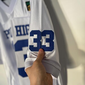 May include: White football jersey with blue and white lettering that reads "PT HIGH" and the number "33" on the sleeve.