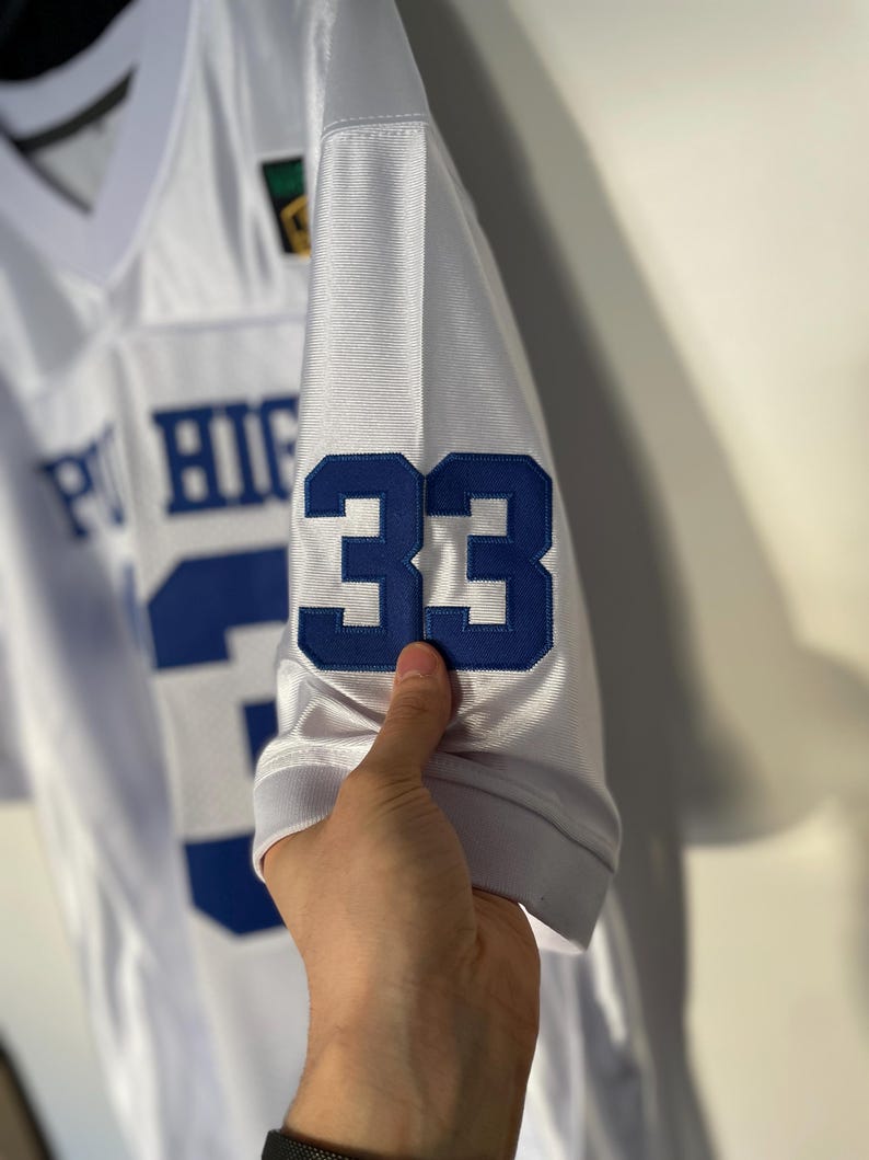 May include: White football jersey with blue and white lettering that reads "PT HIGH" and the number "33" on the sleeve.