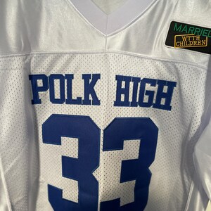 May include: White football jersey with blue lettering that reads "POLK HIGH" and the number "33". A small patch on the right shoulder reads "MARRIED WTH CHILDREN".