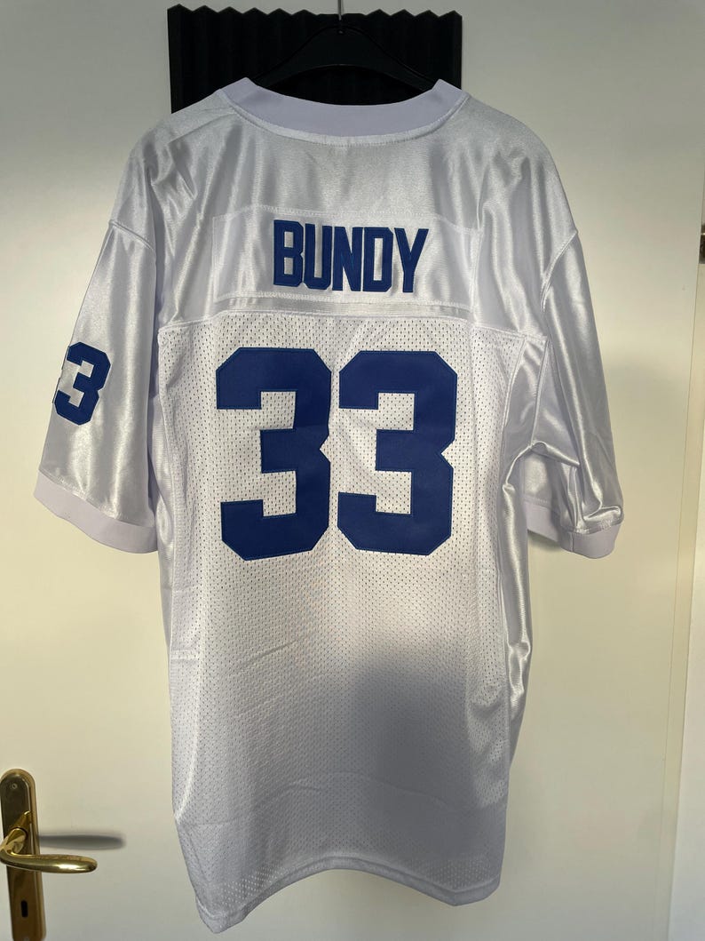 May include: White football jersey with blue lettering on the back. The name "BUNDY" and the number "33" are printed on the back of the jersey.