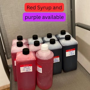 Könnte beinhalten: Eine Auswahl an Plastikflaschen und Behältern, gefüllt mit roten und violetten Flüssigkeiten. Die Behälter haben schwarze Verschlüsse und Etiketten. Der Text auf dem Bild lautet "Red Syrup and purple available."