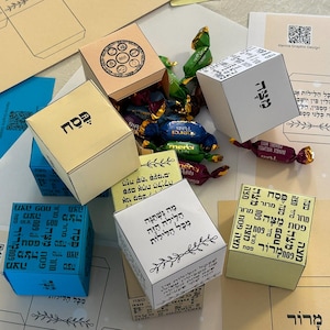 May include: A set of six colourful paper boxes decorated with Hebrew text and Passover symbols. The boxes are filled with small sweets and are ready for a festive celebration.