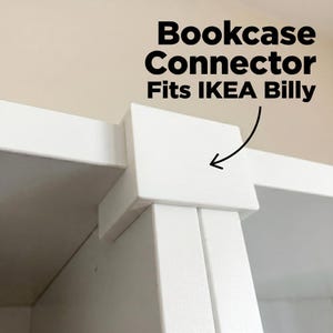 Könnte beinhalten: Ein weißer, quadratischer Bücherregal-Verbinder aus Kunststoff, der zum Verbinden von zwei Regaleinheiten dient. Der Text 'Bookcase Connector Fits IKEA Billy' steht über dem Objekt mit einem Pfeil, der auf das weiße Verbindungsstück zeigt.