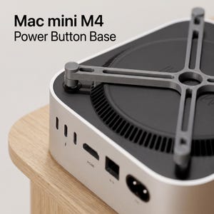 May include: A grey plastic Mac mini M4 Power Button Base attachment featuring a cross-shaped frame that sits atop the computer, with a mechanical arm extending to the power button. The text Mac mini M4 Power Button Base is visible in the image.
