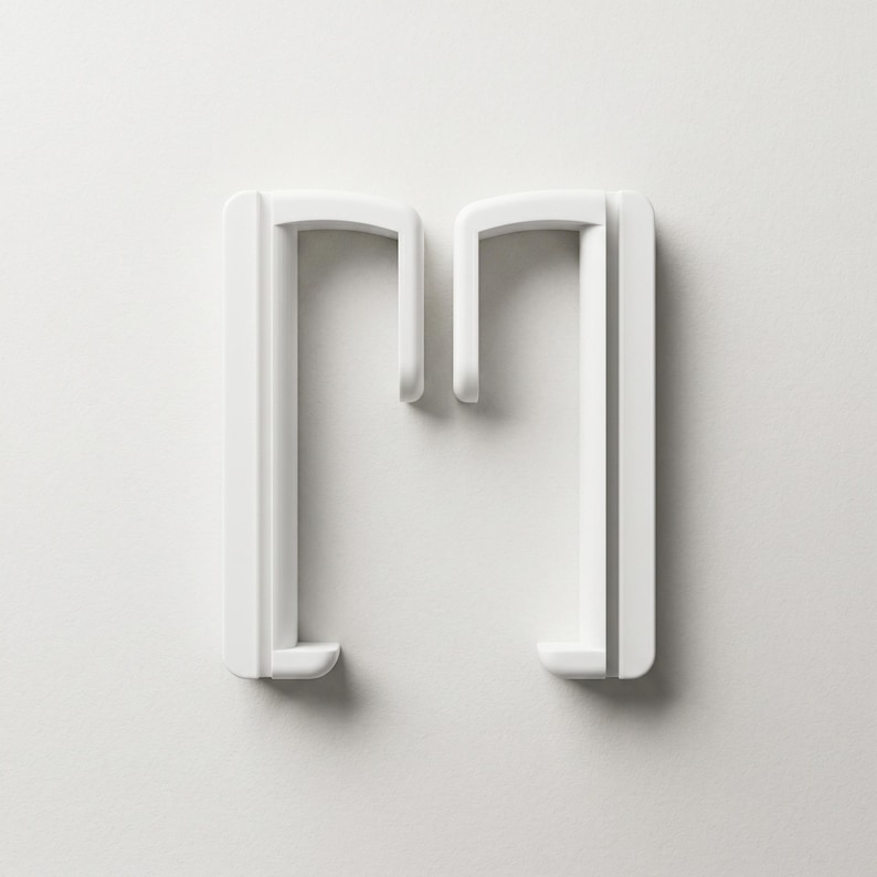 May include: A white, minimalist design element shaped like the letter "M". The object has a clean, modern aesthetic with rounded corners and a smooth surface. The design is set against a plain white background.