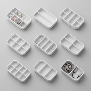 Puede incluir: Nueve bandejas de almacenamiento rectangulares blancas con esquinas redondeadas están dispuestas sobre una superficie gris. Algunas bandejas contienen suministros de costura, joyas y auriculares. Las bandejas tienen varias configuraciones de compartimentos.