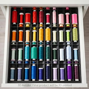 Pode incluir: Um organizador de gavetas de plástico preto contendo fileiras de carretéis de linha de costura coloridos em vários tons, incluindo vermelho, laranja, amarelo, verde, azul, roxo e rosa. O texto na parte inferior diz: 3D Render: Final product will be 3D printed.