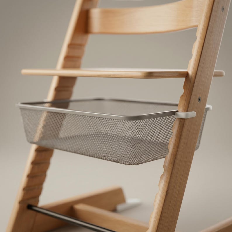 May include: A wooden high chair with a grey metal mesh basket attached. The chair has a natural wood finish and a tray. The basket is rectangular and designed to hold items. The chair is designed for a baby or toddler.