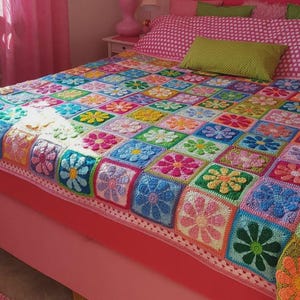 Könnte beinhalten: Ein Schlafzimmer mit einem rosa Bett und Vorhängen sowie einer bunten Häkeldecke. Die Decke zeigt ein Blumenmuster in verschiedenen Farben, darunter Blau, Grün, Gelb und Rosa. Der Raum ist mit rosa Akzenten und einem Fenster dekoriert.