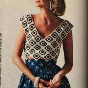 May include: A white and black crocheted top with a V-neck and short sleeves. The top is made of small squares joined together. The model is wearing a blue and white floral skirt.