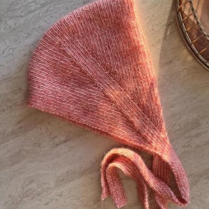 May include: A pink knitted hat with long ties. The hat is made of a soft, fuzzy yarn.