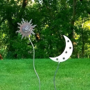 May include: A metal garden sculpture with a sun and moon design. The sun is brown and has a spiral in the center. The moon is white and has stars cut out of it. The sculpture is on a green grassy lawn.