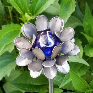 May include: A metal flower sculpture with a blue and white marble in the center. The flower has many petals that are silver in color.