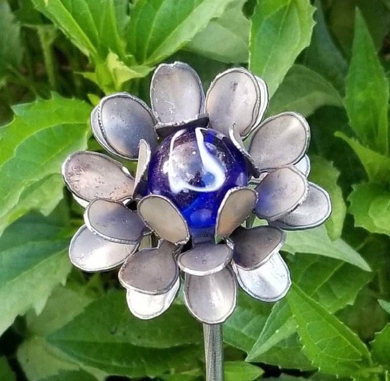 May include: A metal flower sculpture with a blue and white marble in the center. The flower has many petals that are silver in color.