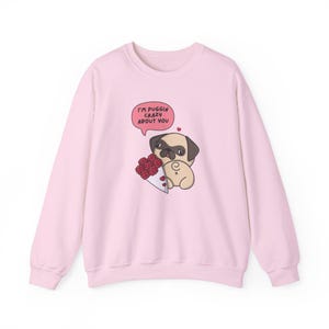 May include: Pink sweatshirt with a cartoon pug holding a bouquet of red roses. The text "I'm puggin' crazy about you" is in a speech bubble above the pug.