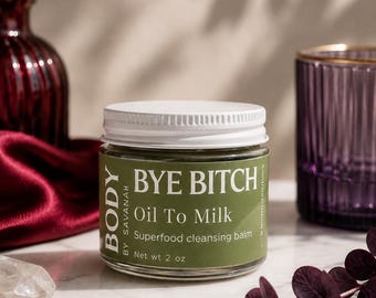 May include: A clear glass jar with a white screw-top lid containing a cleansing balm. The green label features the white text "BODY BY SAVANAH", "BYE BITCH", "Oil To Milk", "Superfood cleansing balm", and "Net wt 2 oz" in a clean sans-serif font.