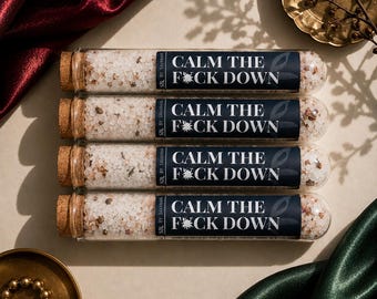 May include: Four clear glass test tubes filled with coarse pink and white bath salts, each sealed with a cork stopper. A dark blue label on each tube features the white text CALM THE F*CK DOWN, with SBL BY SAVANNAH printed vertically on the side.