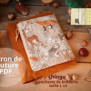May include: A brown leather pouch with a zipper closure and a colorful fabric lining featuring a woodland animal print. The fabric lining has a pattern of deer, owls, foxes, and mushrooms. The pouch is labeled "chingu pochette de broderie taille L v2".