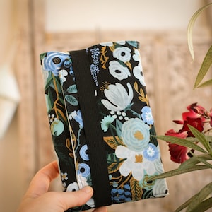 May include: A black fabric pouch with a floral pattern in shades of blue, green, and yellow. The pouch has a black strap and a zipper closure.