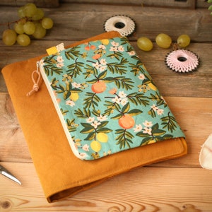 May include: A mustard yellow fabric notebook cover with a zippered pouch. The pouch is made of a light blue fabric with a floral pattern of white flowers, green leaves, and orange citrus fruit.