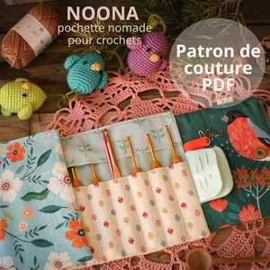 May include: A green, blue, and pink crochet project bag with a floral pattern and a bird design. The bag has a zipper closure and a strap for carrying. The bag is filled with crochet hooks and a needle case. The bag is on a crocheted doily. The text "NOONA pochette nomade pour crochets Patron de couture PDF" is visible on the image.