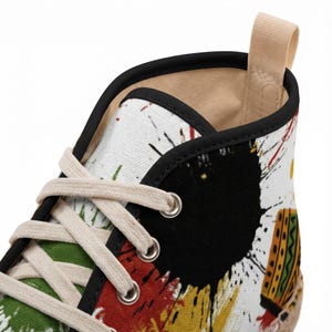 Puede incluir: Zapatilla alta de lona con un diseño abstracto colorido. El zapato presenta una base blanca con salpicaduras de pintura negra, roja, amarilla y verde. Tiene cordones beige y un ribete negro.