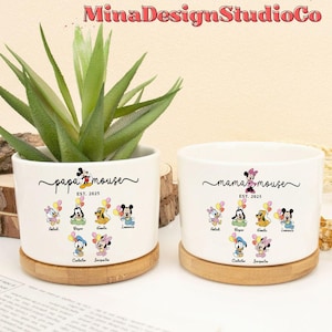 May include: Two white ceramic planter pots with a wooden base. The pots feature a black and white illustration of Mickey Mouse and Minnie Mouse with their children. The text on the pots reads "papa mouse EST. 2025" and "mama mouse EST. 2025".