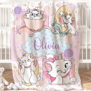 May include: A pink and white fleece blanket with a cartoon cat design. The blanket features a cat in a teacup, a cat with a ball of yarn, and a cat with a makeup brush. The blanket also has the name "Olivia" written on it.
