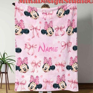 Puede incluir: Manta de forro polar rosa con un patr&oacute;n repetido de cabezas de Minnie Mouse y lazos rosas. La manta tiene la palabra "NAME" impresa en el centro.