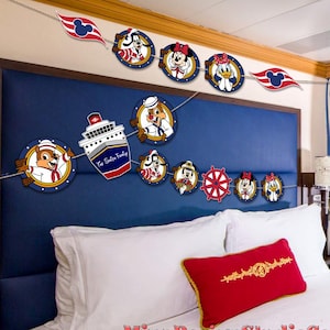 May include: A festive banner featuring Disney characters and nautical elements. The banner includes circular cutouts with characters like Mickey Mouse, Minnie Mouse, and Donald Duck, along with a ship and a ship's wheel. The banner is strung across a blue headboard.