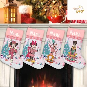 May include: Four pink Christmas stockings with Disney characters, including Mickey Mouse, Minnie Mouse, and Goofy, are displayed. Each stocking has a pink top with the word "NAME" printed on it. The stockings are decorated with snowflakes and Christmas trees.