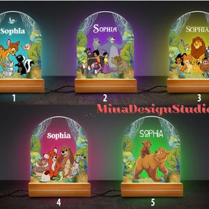 May include: Five different night light designs featuring Disney characters. Each light has a wooden base and a clear acrylic panel with a colorful image. The images include characters from The Lion King, The Jungle Book, and Bambi. The name "Sophia" is printed on each light.