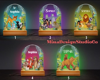 May include: Five different night light designs featuring Disney characters. Each light has a wooden base and a clear acrylic panel with a colorful image. The images include characters from The Lion King, The Jungle Book, and Bambi. The name "Sophia" is printed on each light.