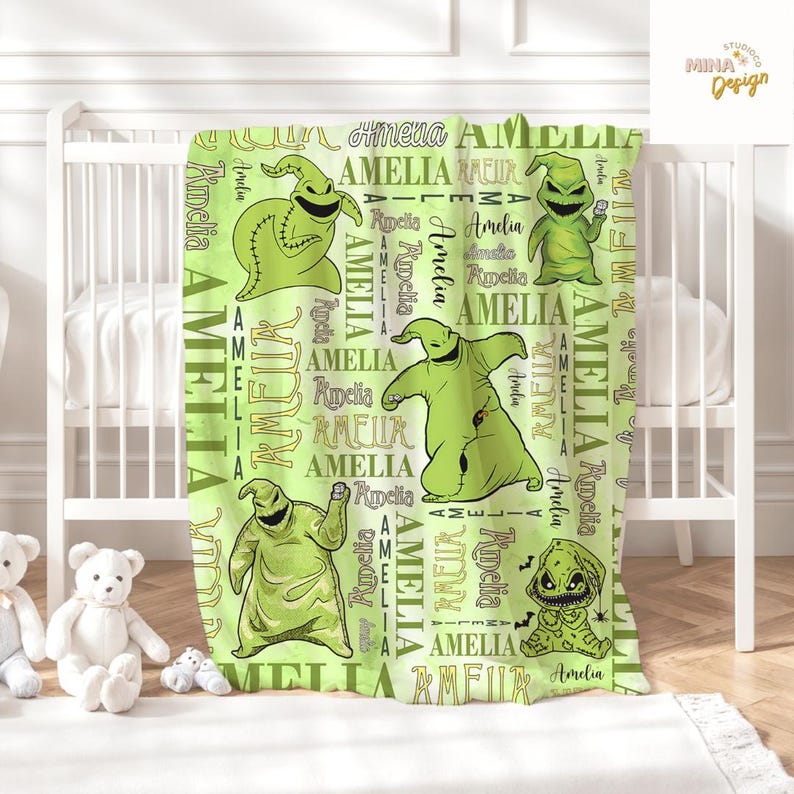 May include: A light green baby blanket featuring cartoon characters and the name "Amelia" in a repeating pattern. The blanket has a white border and is displayed on a white crib.