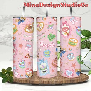 K&ouml;nnte beinhalten: Drei rosafarbene Edelstahlbecher mit einem rosa-wei&szlig;en Muster mit Figuren aus dem Film Toy Story. Die Becher haben einen Strohhalm und der Name "Sophia" steht auf dem mittleren Becher.