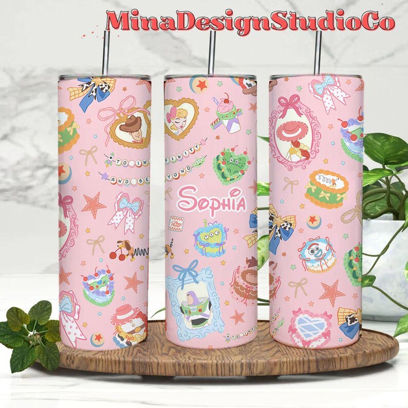 K&ouml;nnte beinhalten: Drei rosafarbene Edelstahlbecher mit einem rosa-wei&szlig;en Muster mit Figuren aus dem Film Toy Story. Die Becher haben einen Strohhalm und der Name "Sophia" steht auf dem mittleren Becher.
