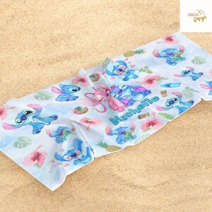 May include: A white beach towel featuring a repeating pattern of the character Stitch from the animated film Lilo & Stitch. The design includes Stitch in various poses, pink hibiscus flowers, and pineapples. The name "Michelle" is printed in blue script.