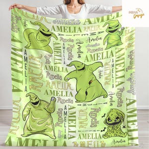 May include: A light green blanket featuring multiple cartoon images of Oogie Boogie from The Nightmare Before Christmas. The blanket has the name "Amelia" printed repeatedly in various fonts and sizes.
