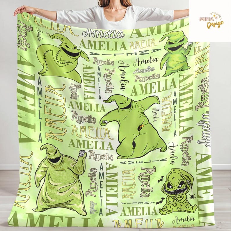 May include: A light green blanket featuring multiple cartoon images of Oogie Boogie from The Nightmare Before Christmas. The blanket has the name "Amelia" printed repeatedly in various fonts and sizes.