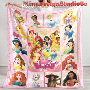 Puede incluir: Manta de forro polar rosa con un collage de princesas Disney, incluyendo Cenicienta, Ariel, Bella y Moana. La manta tiene un fondo rosa con estrellas blancas y el nombre "Sophia" en una fuente decorativa.