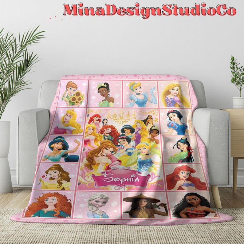 Puede incluir: Manta de forro polar rosa con un collage de princesas Disney, incluyendo Cenicienta, Blancanieves, Ariel y Bella. La manta tiene un fondo rosa con un borde blanco y el nombre "Sophia" en una pancarta blanca.