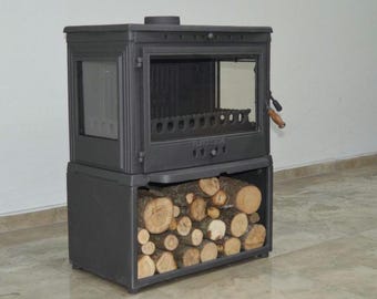 May include: A black cast iron wood-burning stove with a glass door and a wood storage compartment below. The stove has a handle on the right side and a label that reads "PLANIKA".