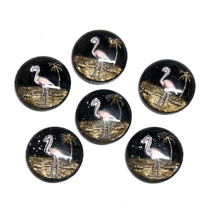 May include: Set of six black buttons with a flamingo and palm tree design. Each button features a pink flamingo standing on gold-colored grass, with a palm tree silhouette. The buttons are round and have a glossy finish.