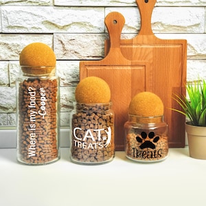 three jars of cat treats next to a cutting board