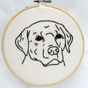 Könnte beinhalten: Ein bestickter weißer Stoffring mit einer schwarzen Linienzeichnung eines Labrador Retriever-Kopfes. Die Augen des Hundes sind braun.