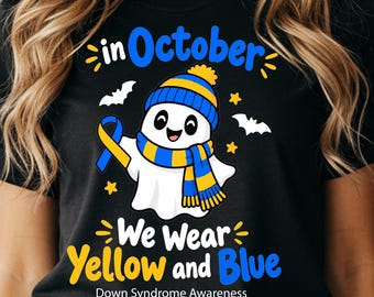 Può includere: Una t-shirt nera con un personaggio fantasma bianco che indossa un berretto e una sciarpa a righe blu e gialle. La grafica include il testo "in October We Wear Yellow and Blue" e "Down Syndrome Awareness" con stelle e pipistrelli gialli.