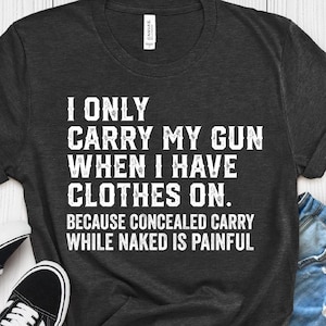 Könnte beinhalten: Ein dunkelgraues Kurzarm-T-Shirt mit weißem Text: I ONLY CARRY MY GUN WHEN I HAVE CLOTHES ON. BECAUSE CONCEALED CARRY WHILE NAKED IS PAINFUL. Das T-Shirt wird zusammen mit schwarz-weißen Turnschuhen und blauen Jeansshorts präsentiert.