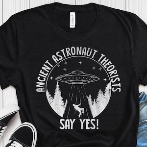 May include: Black t-shirt with a white circle graphic featuring a UFO, trees, and the text "Ancient Astronaut Theorists Say Yes!"