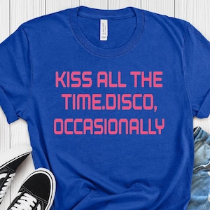 Pode incluir: Uma camiseta azul True Royal com o texto "KISS ALL THE TIME. DISCO, OCCASIONALLY" em rosa. A camiseta é combinada com shorts jeans e tênis preto e branco. A camiseta é feita de um material macio.
