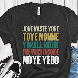 May include: A dark grey t-shirt with a vintage-style graphic design featuring the text "Jone waste yore Toye Monme Yorall Rediii The voice insoide Moye Yedd".